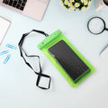 A bright green clear phone pouch with a black lanyard holds a black smartphone on a light blue desk with a silver laptop,