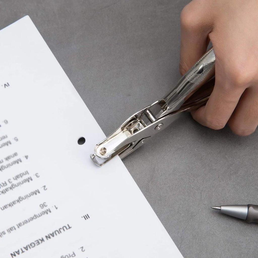 Handheld metal hole puncher in action, cleanly punching through paper.