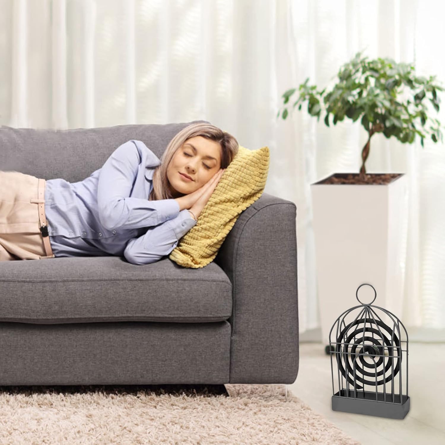 A black iron birdcage-style holder with a mosquito coil sits on a rug next to a gray sofa where a person is sleeping.