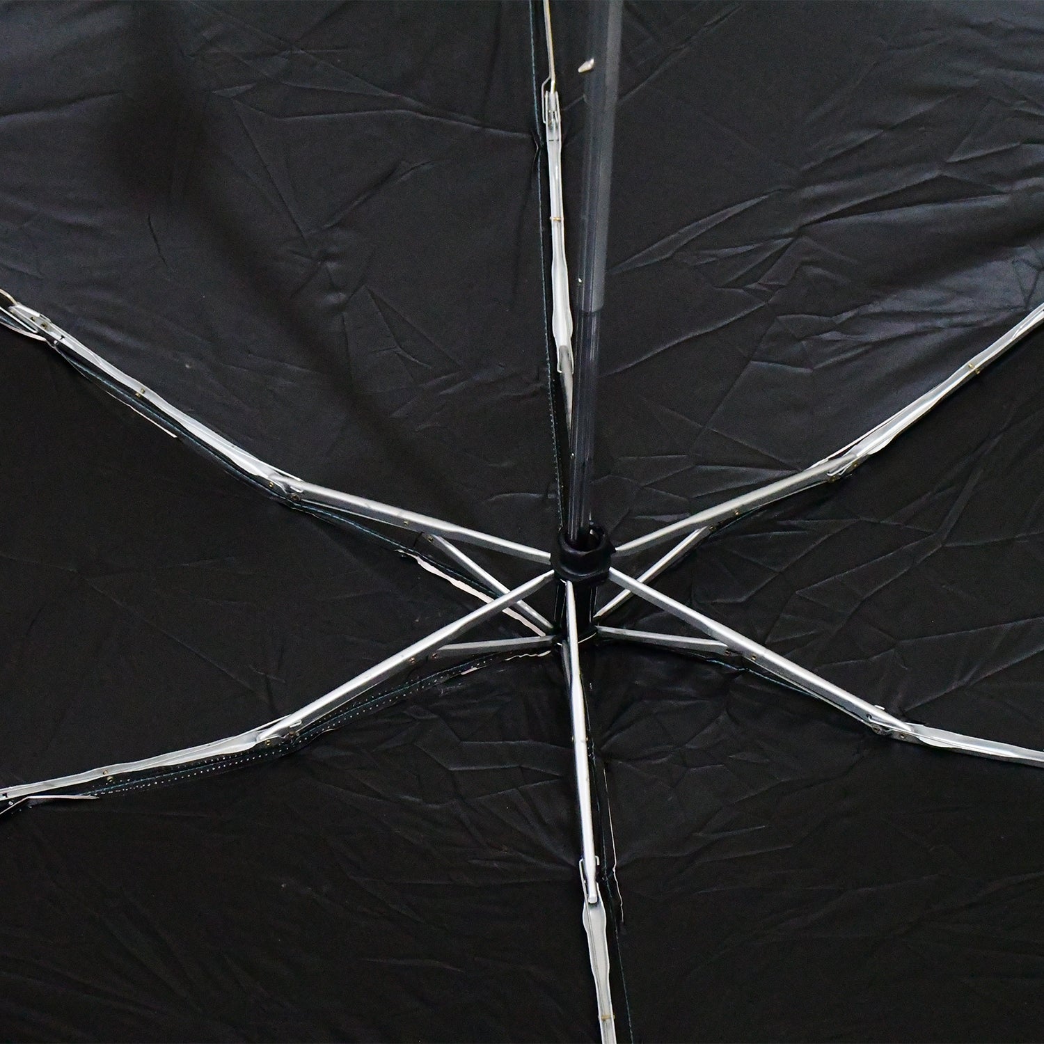The interior of a black umbrella reveals its silver metal spokes and central mechanism.