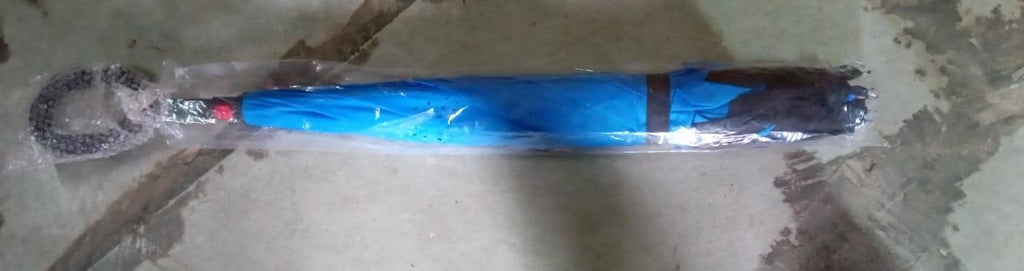 A blue and black umbrella, still in its clear plastic packaging, lies horizontally on a textured surface.